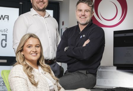 2 males stood up and 1 female sat down in business attire at a digital design agency