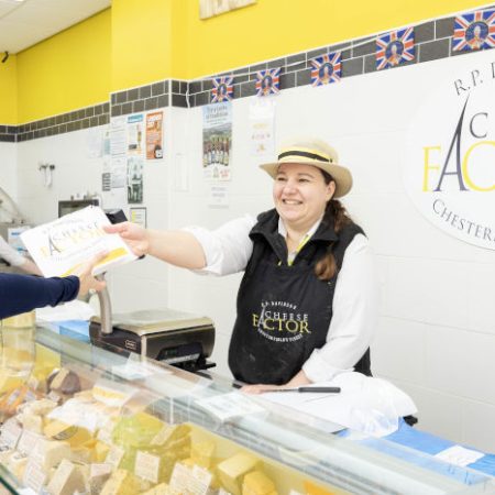 Cheese Factor female team member serving cheese in a paper bag to a female customer