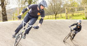 Rider on bmx bike on slanted track, another rider in background