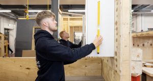 White male joinery student in blue overalls, using a spirit level