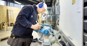 White student joiner using power tool, wearing white cap and earphones