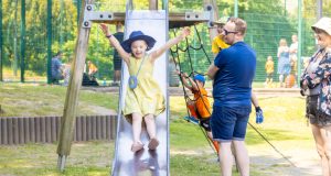 Young female in yellow dress and blue hat sliding down metal slide