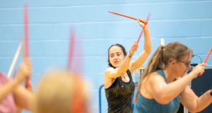 White female instructor in sports gear leading a class with dance sticks in air