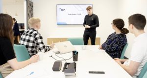 Group of business people at table listening to young male presenting in front of a screen with PowerPoint at BHP, 1 Waterside Place, Chesterfield