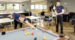 Two males playing pool in the staff room at Central Technology, Dunston, women at table in the background