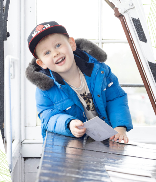 Boy in blue coat and black cap smiling