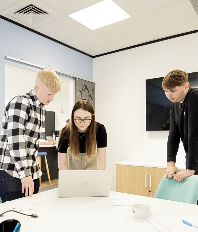 Group of business trainees looking at a laptop in meeting room