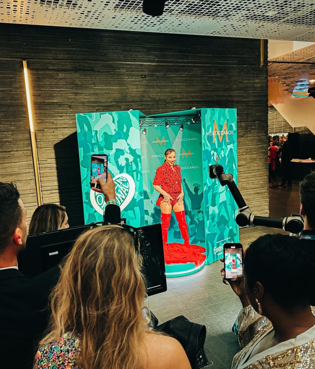 Woman in red outfit stood in blue photo booth posing for robotic camera arm