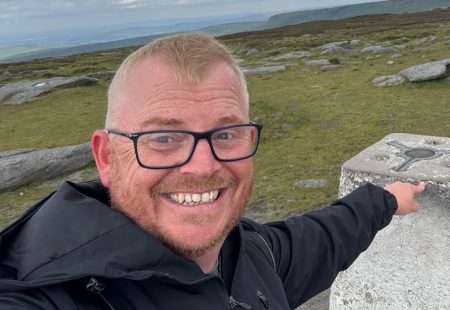 Jim Edgar, director of Methodolgy man Ltd, Man with glasses touching a trig point