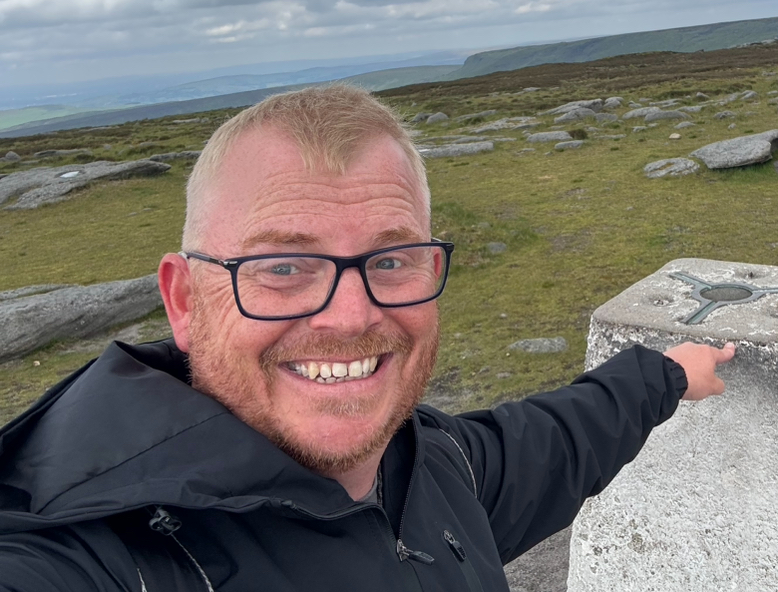 Jim Edgar, director of Methodolgy man Ltd, Man with glasses touching a trig point