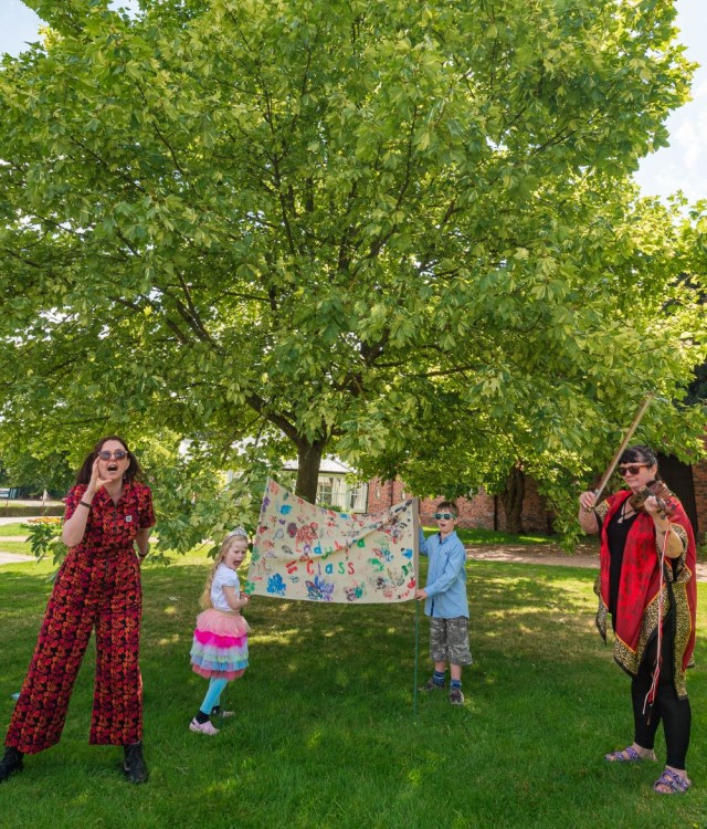 Adults and children holding banner under tree